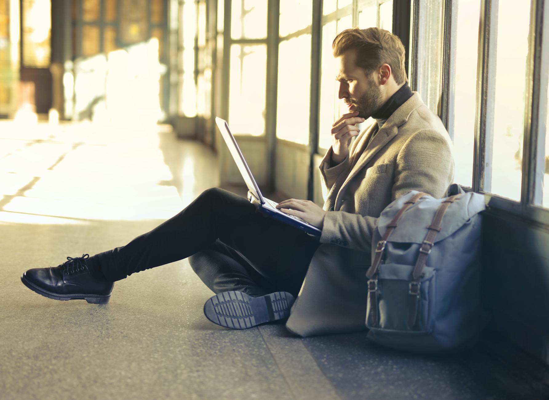 Young man sitting indoors at an airport using laptop. Ideal for remote work themes.