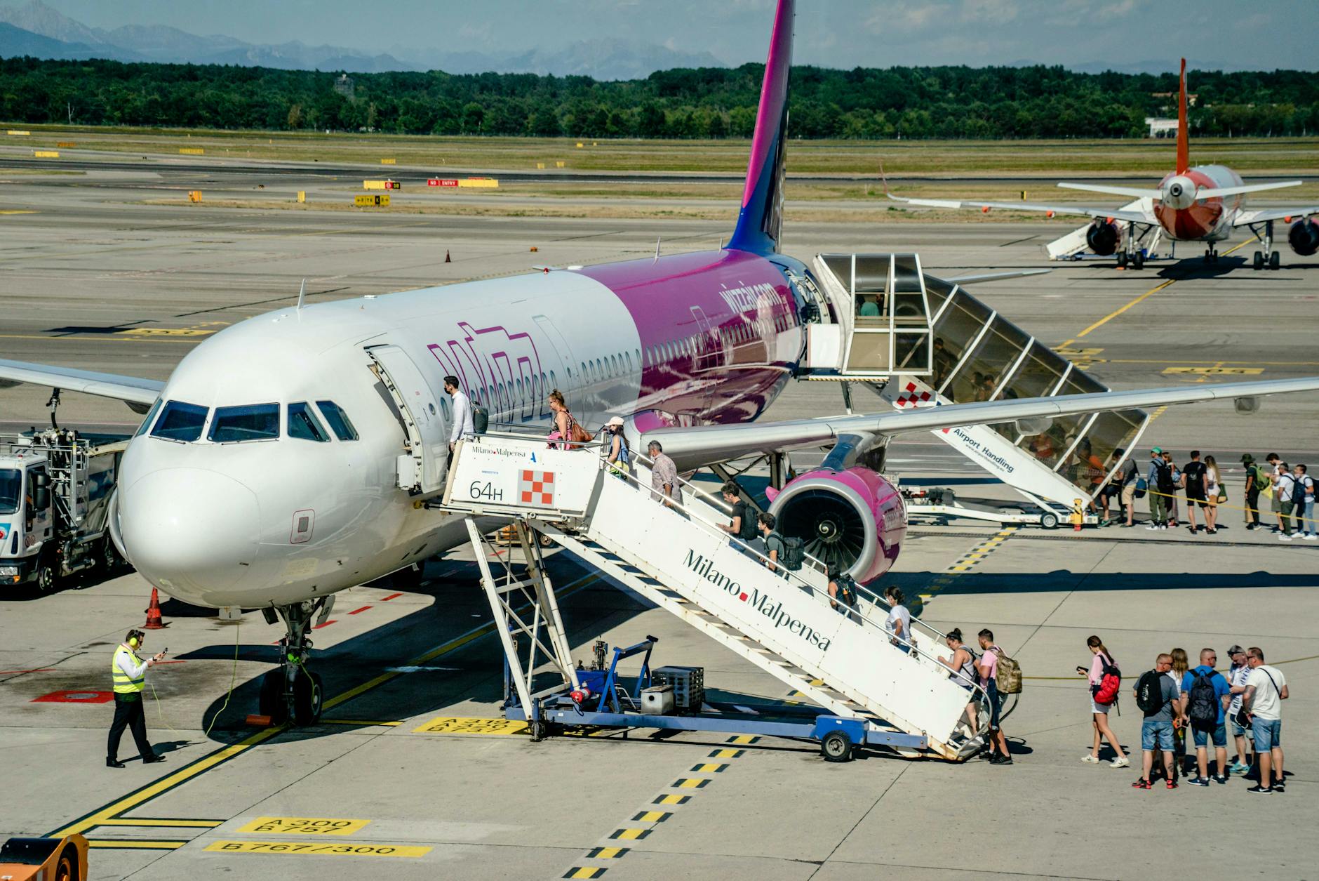 Travelers board an airplane at Milan Malpensa Airport on a sunny day, showcasing modern air travel.