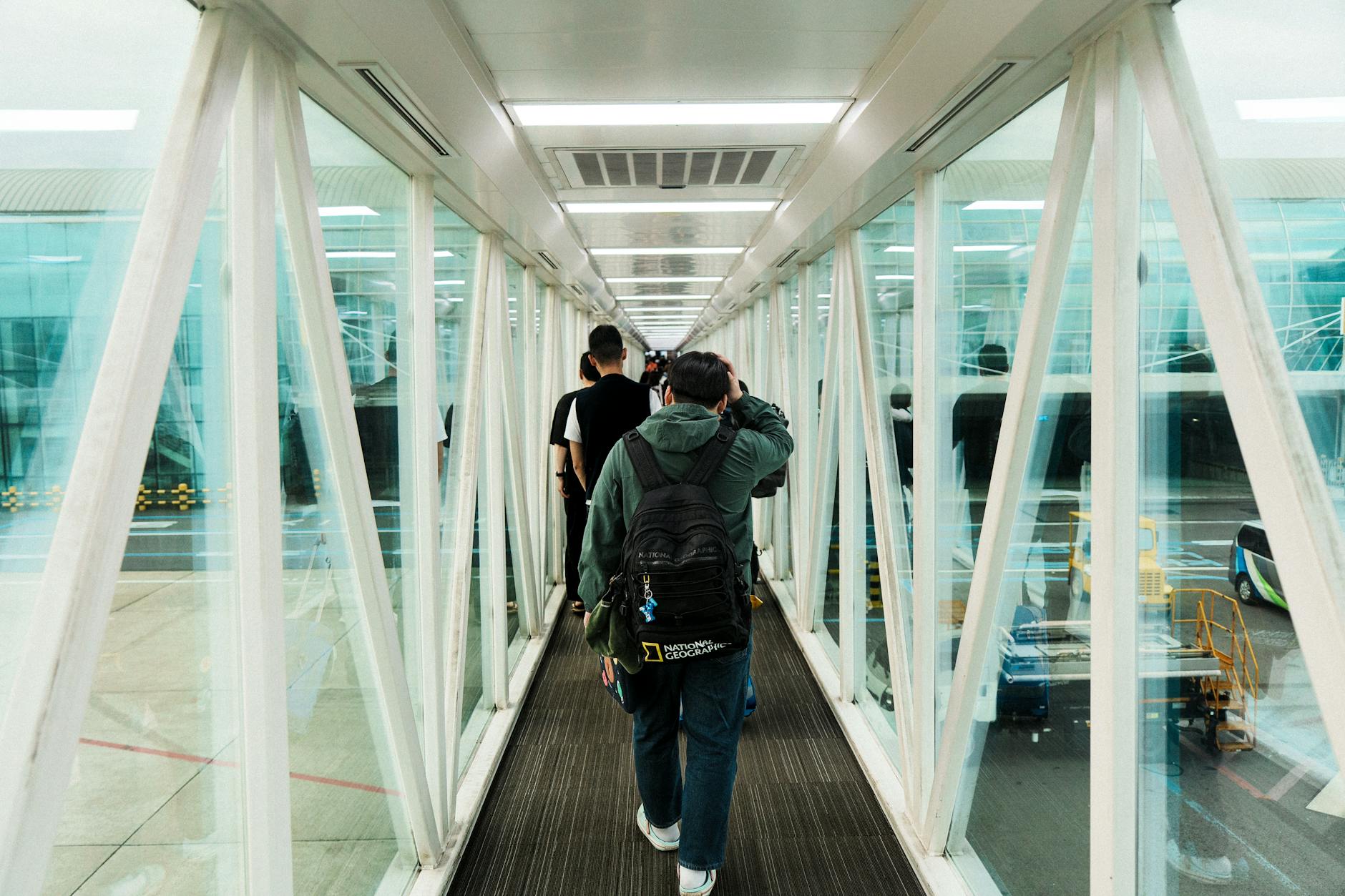 Travelers moving through a modern glass jet bridge at an airport, capturing urban transit dynamics.