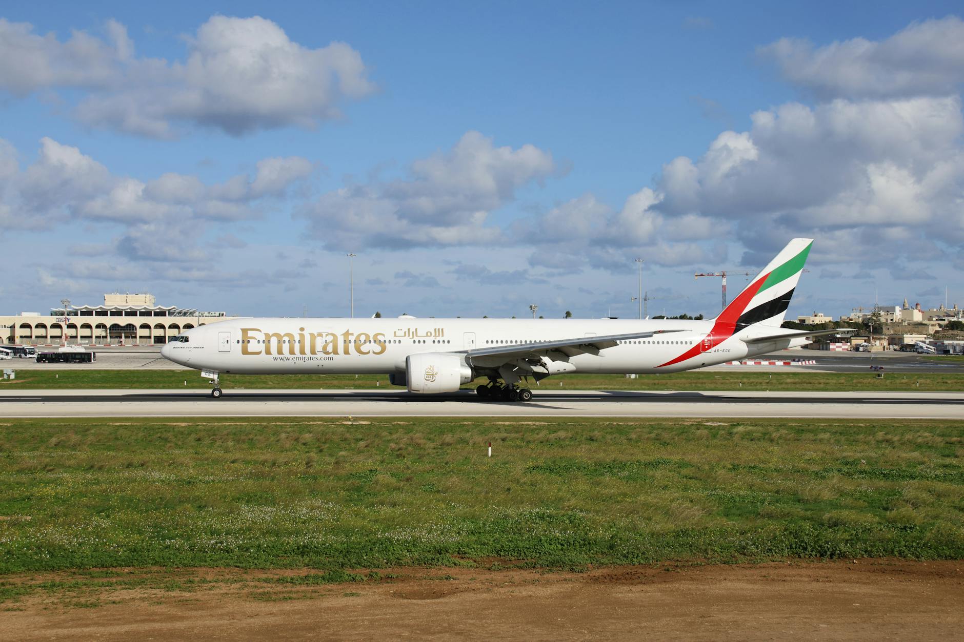 Emirates airplane parked on a sunny day at an airport runway under blue skies.