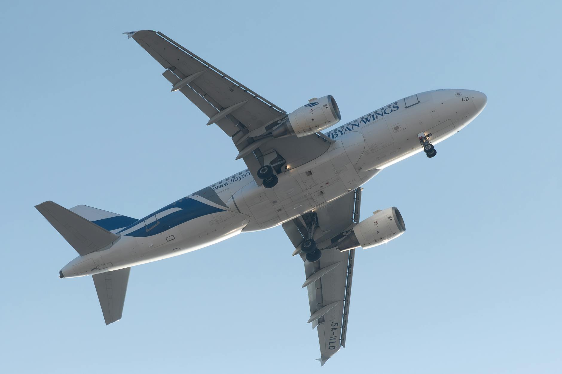 Airplane in flight captured from below against a clear sky backdrop.
