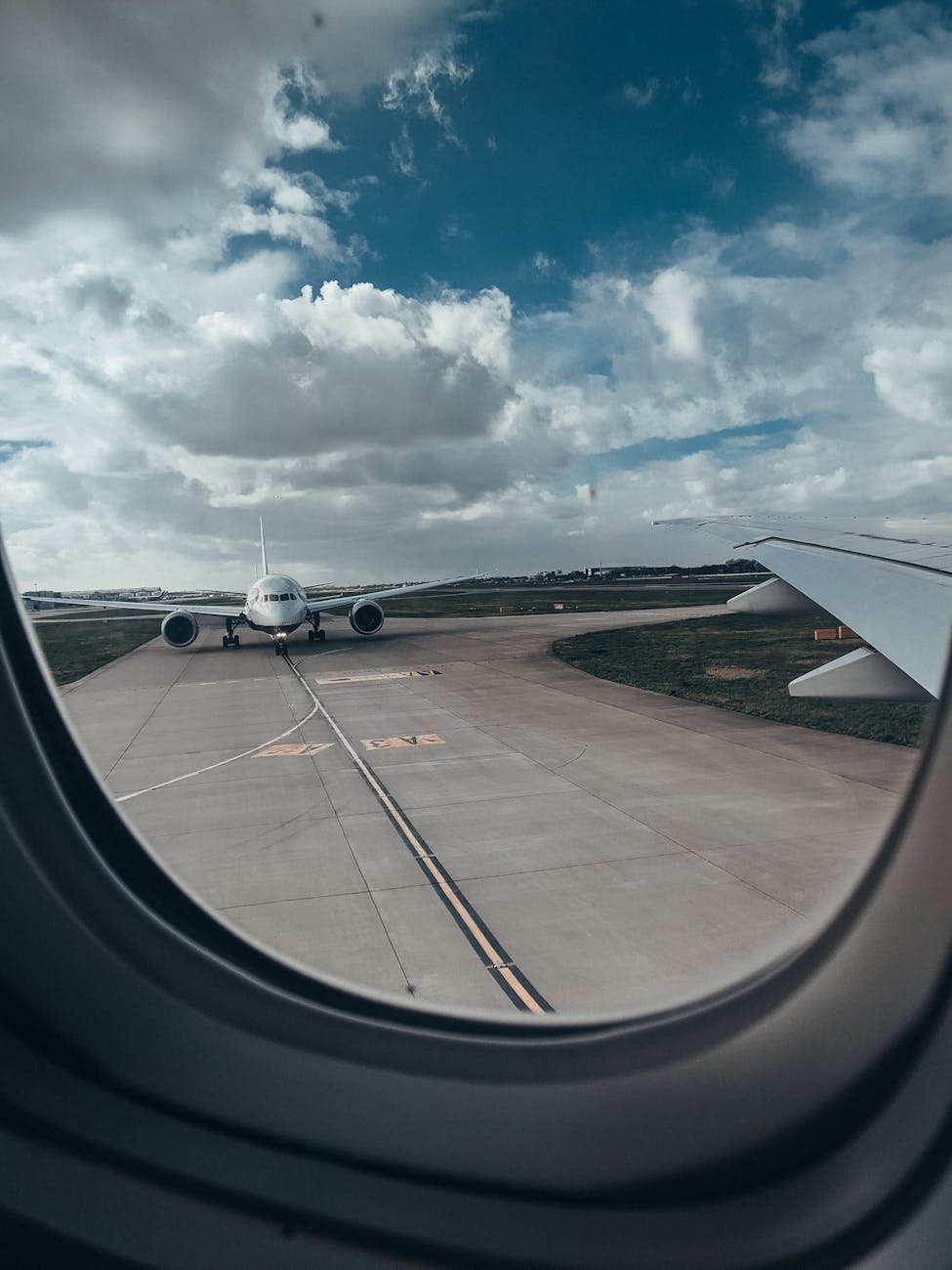 View from an airplane window showing another aircraft on a tarmac under cloudy skies.