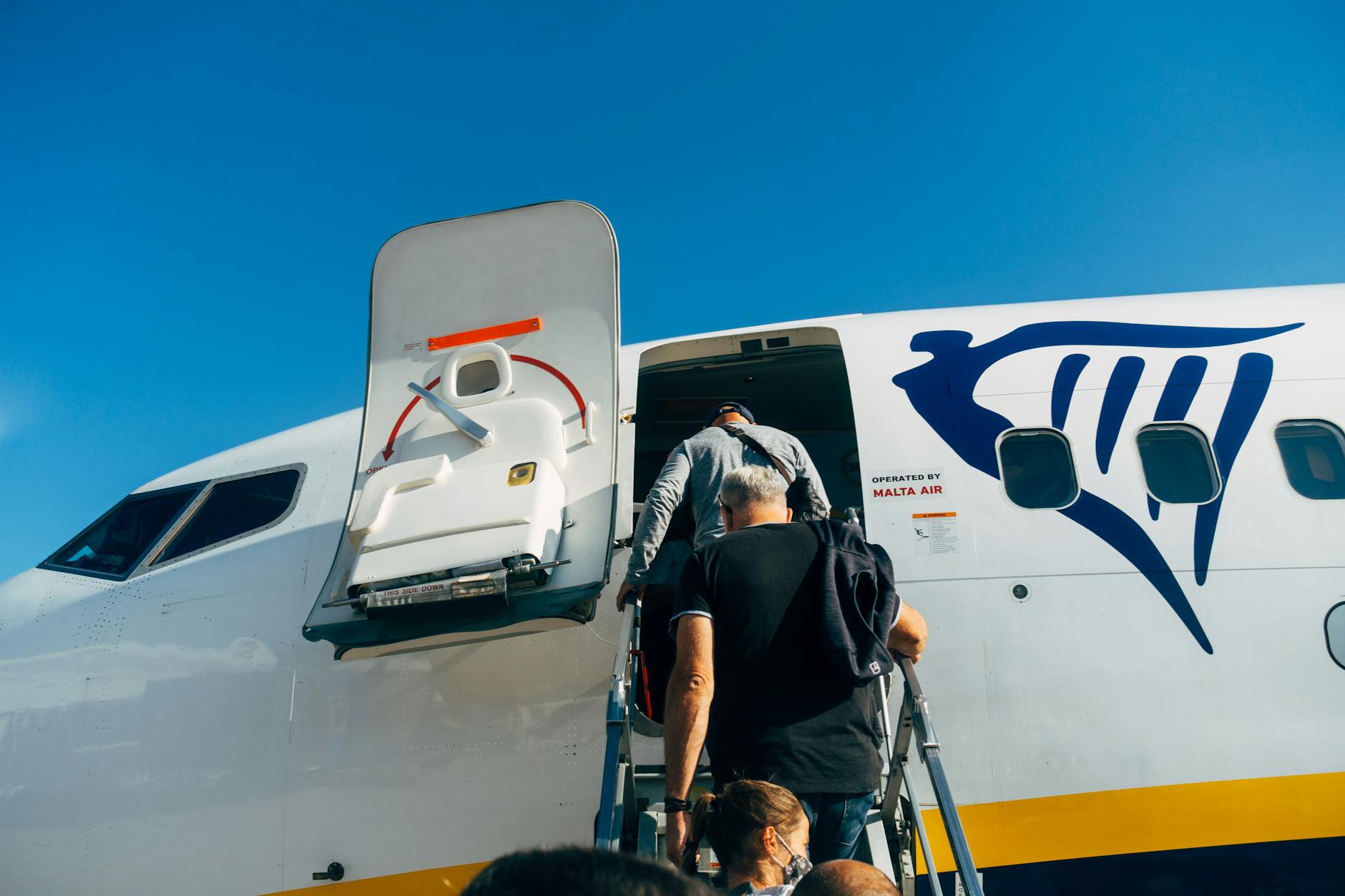 Travelers board a Ryanair plane for their flight under a clear blue sky.