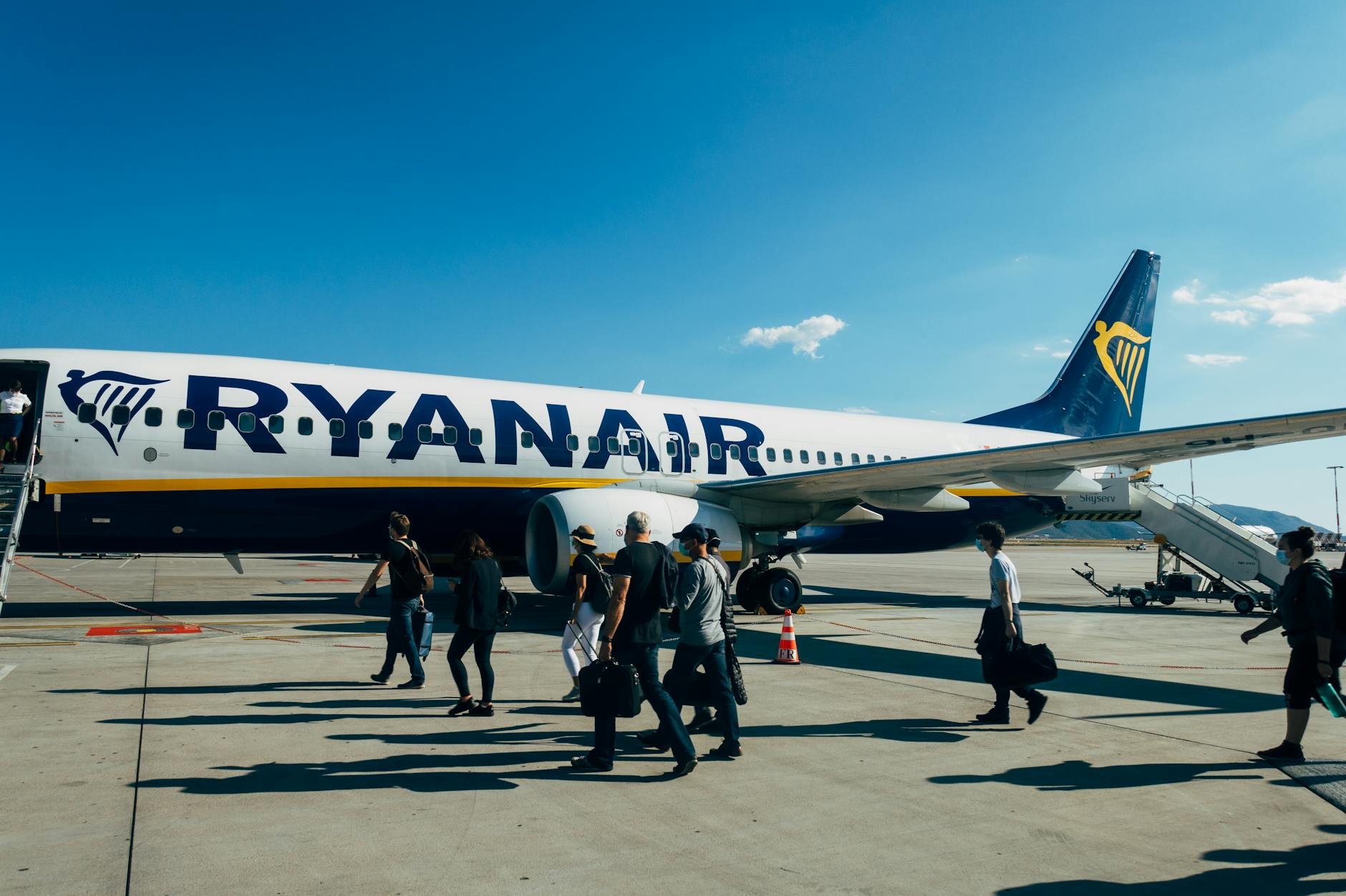 Travelers boarding a Ryanair airplane under clear blue sky at the airport.