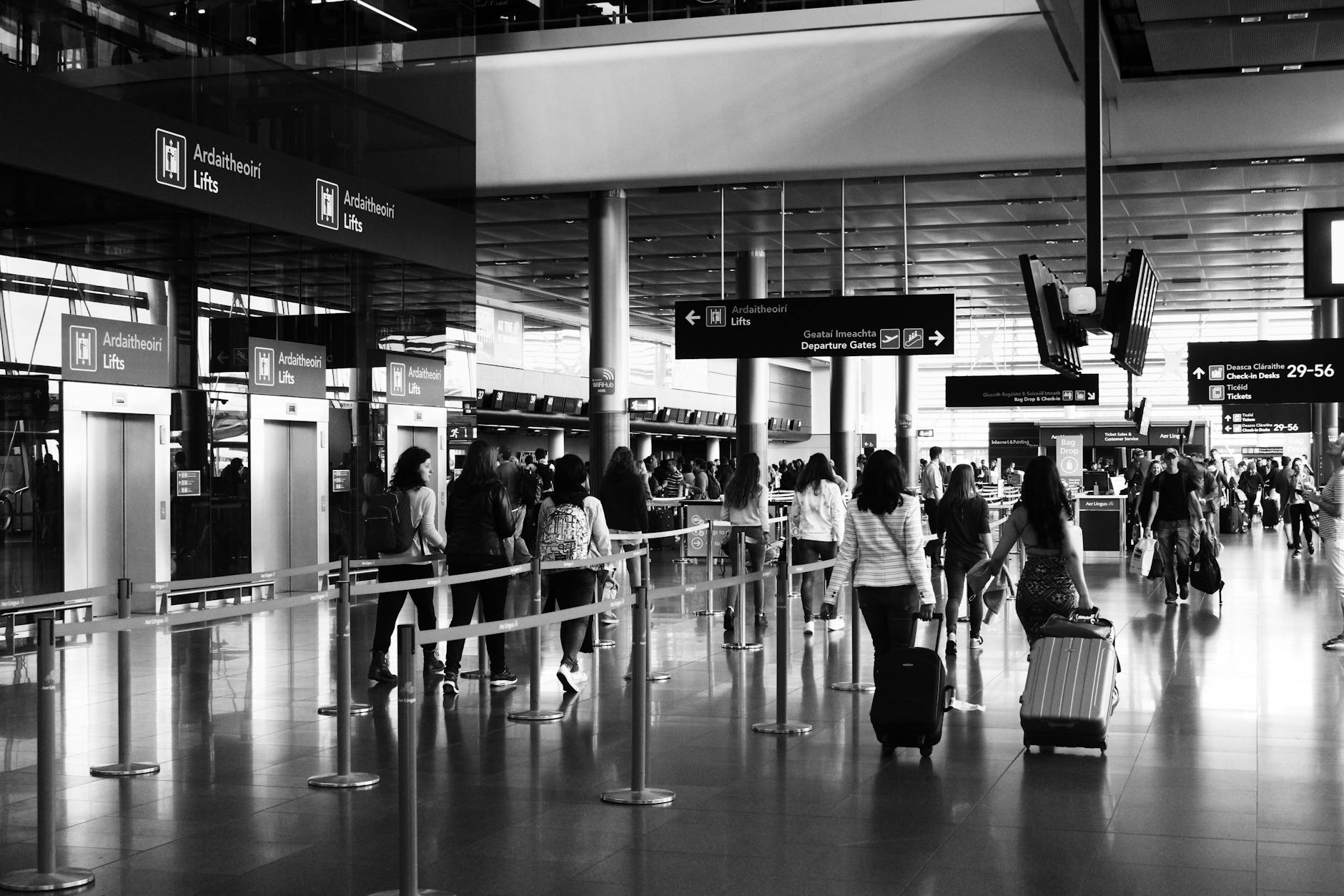 Black and white photo of travelers walking with luggage in a bustling airport terminal.