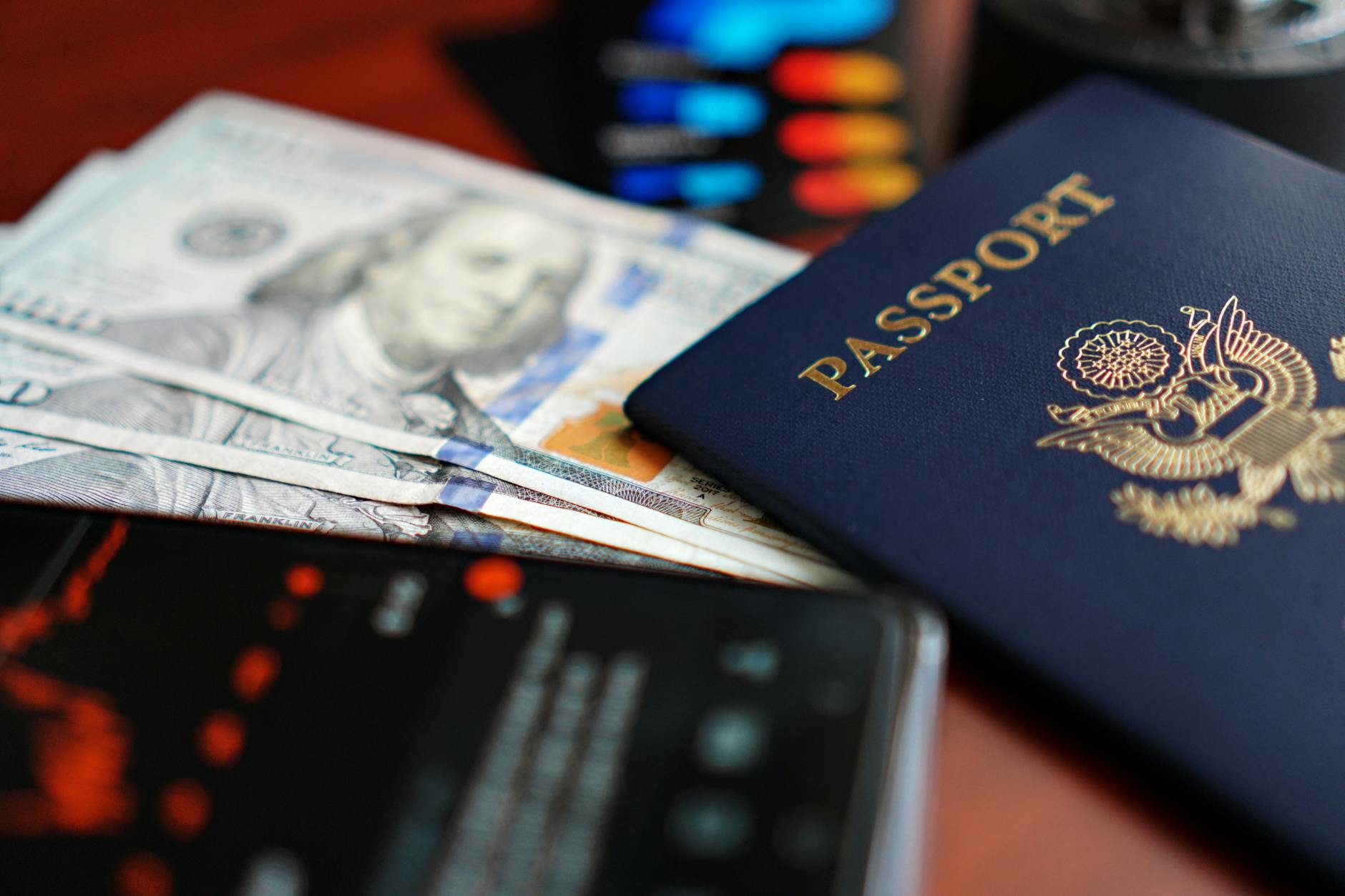 A close-up image of a U.S. passport, dollar bills, and a smartphone.