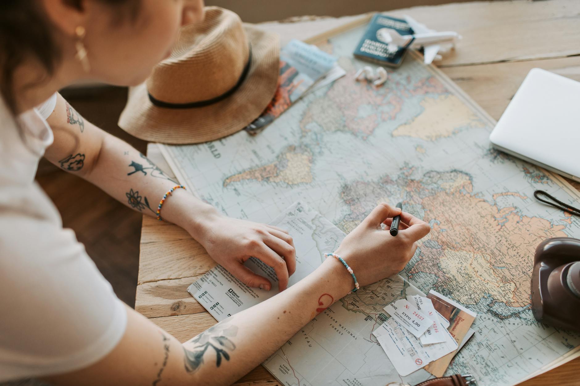 Person planning a journey with a map, passport, and travel essentials on a wooden table.