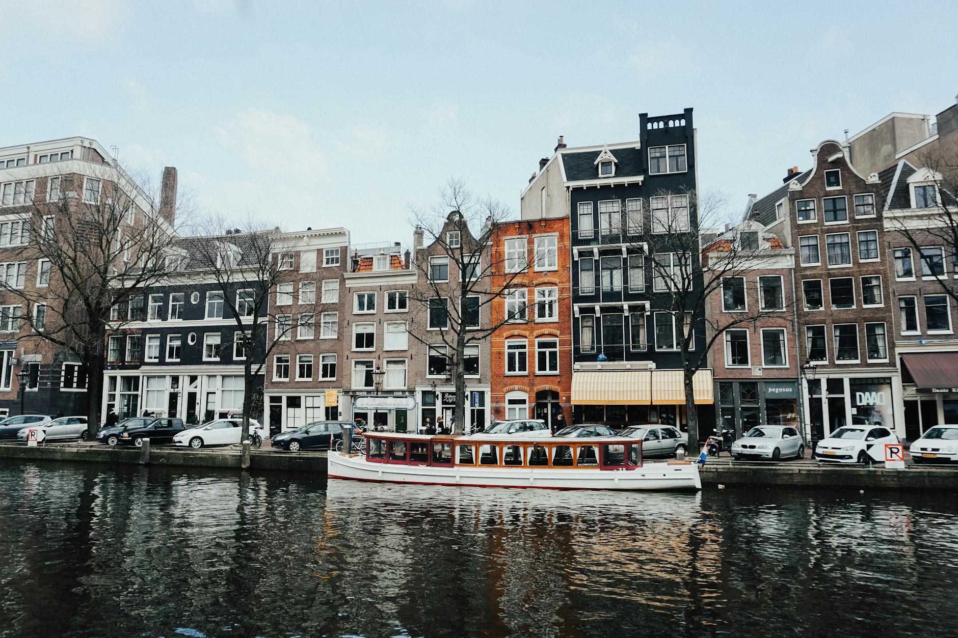 Charming Amsterdam canal scene with classic Dutch architecture and a boat cruising on the water.