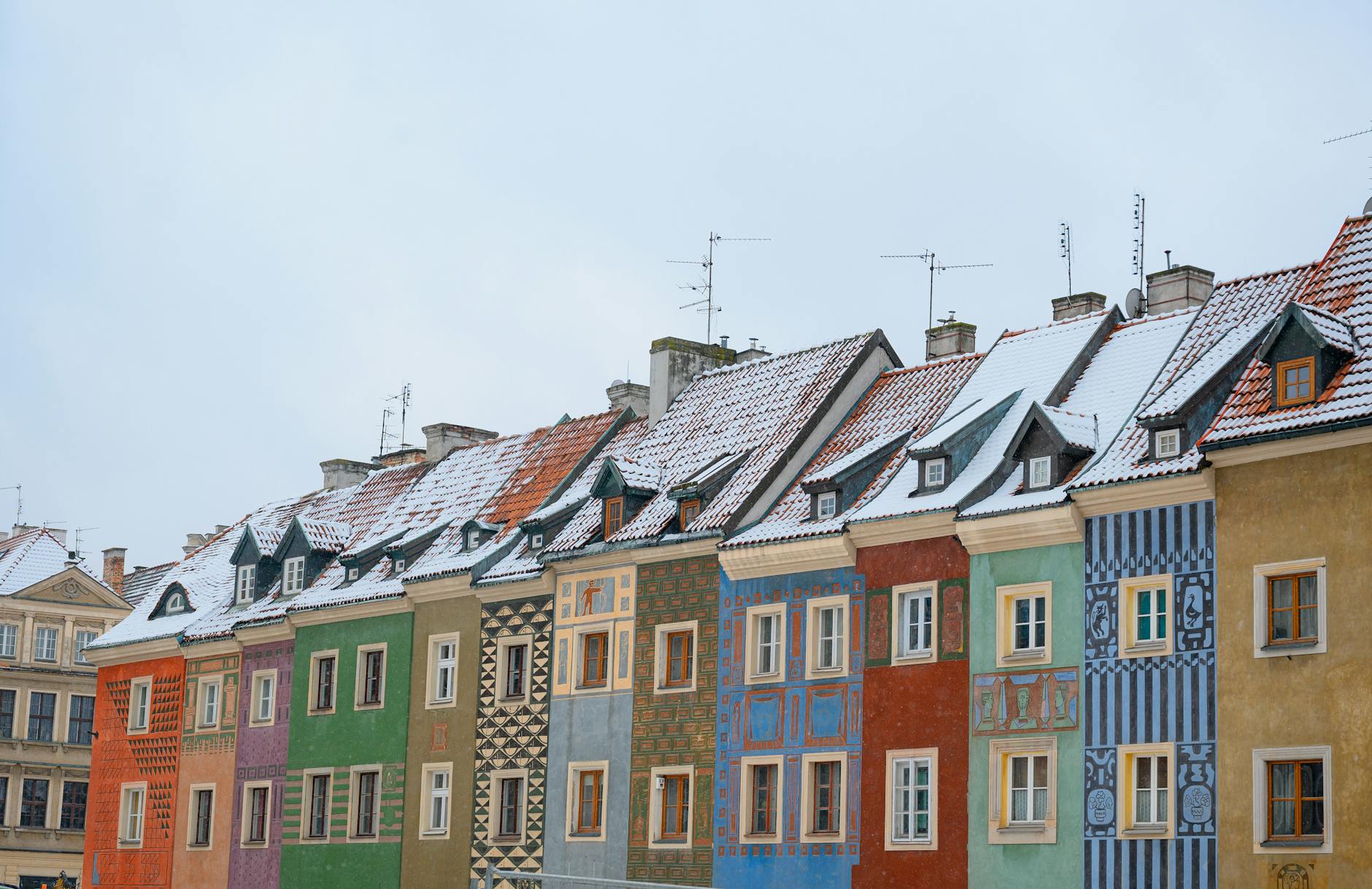 A row of vibrant, historic houses with snowy rooftops in a European town, showcasing unique architectural styles.