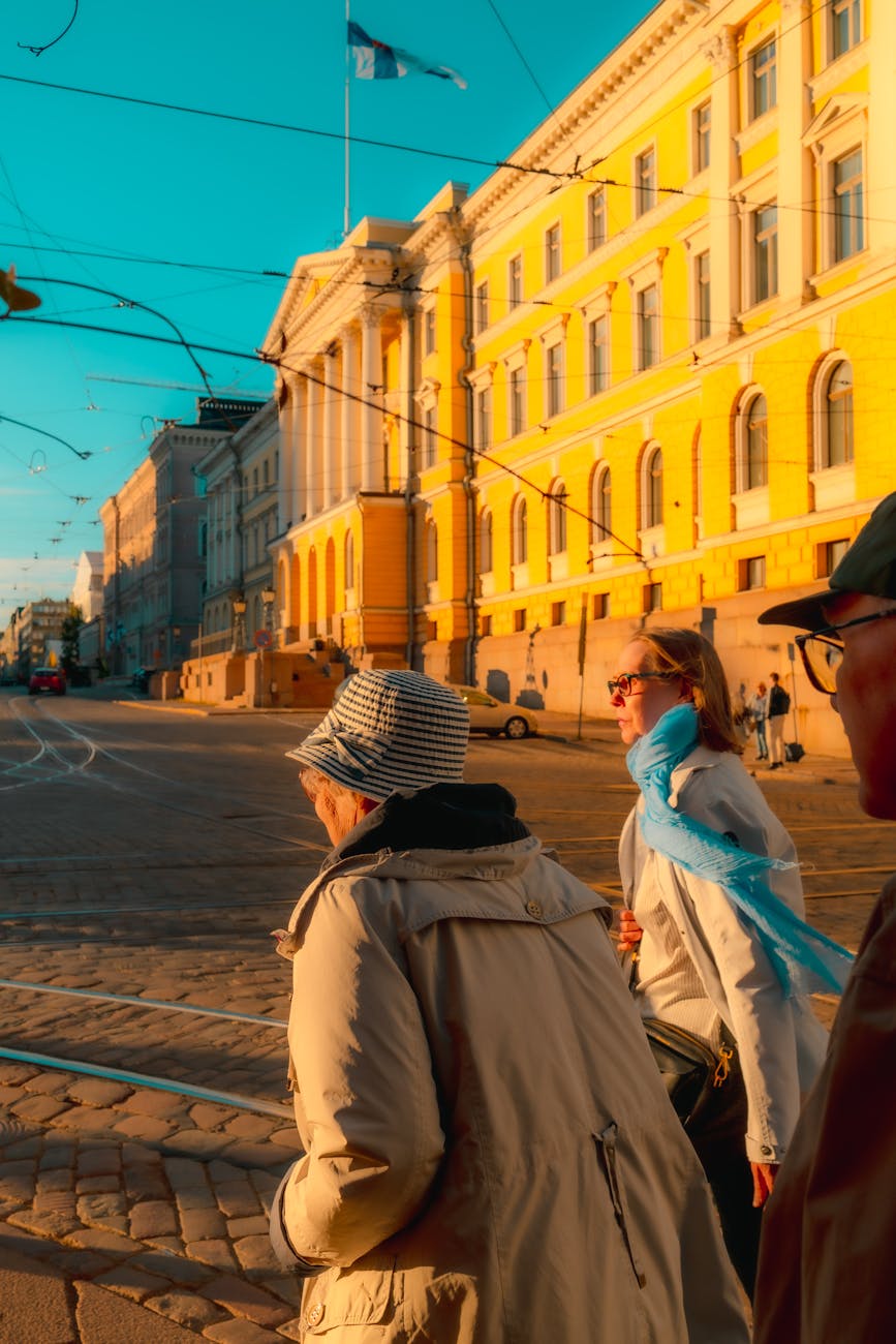 Pedestrians walk through a sunlit street near Helsinki's historic architecture.