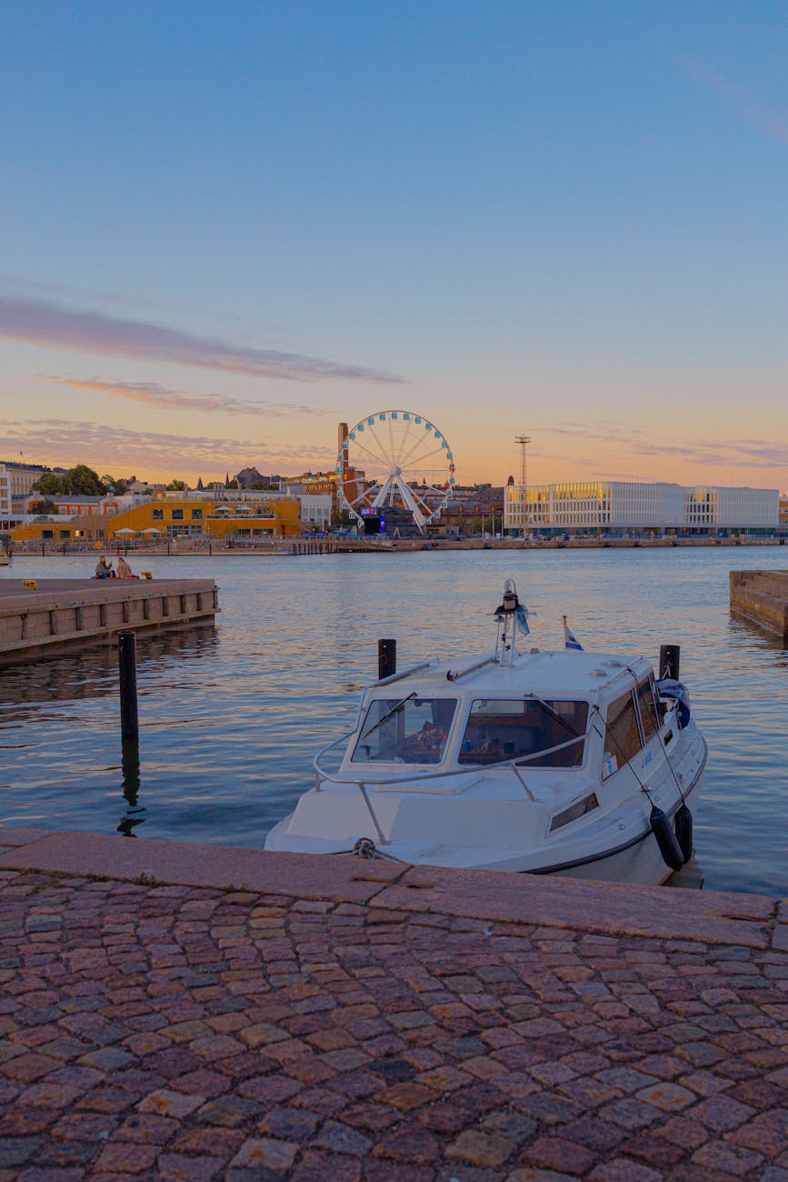 Scenic view of Helsinki harbor at sunset, featuring a boat and Ferris wheel.