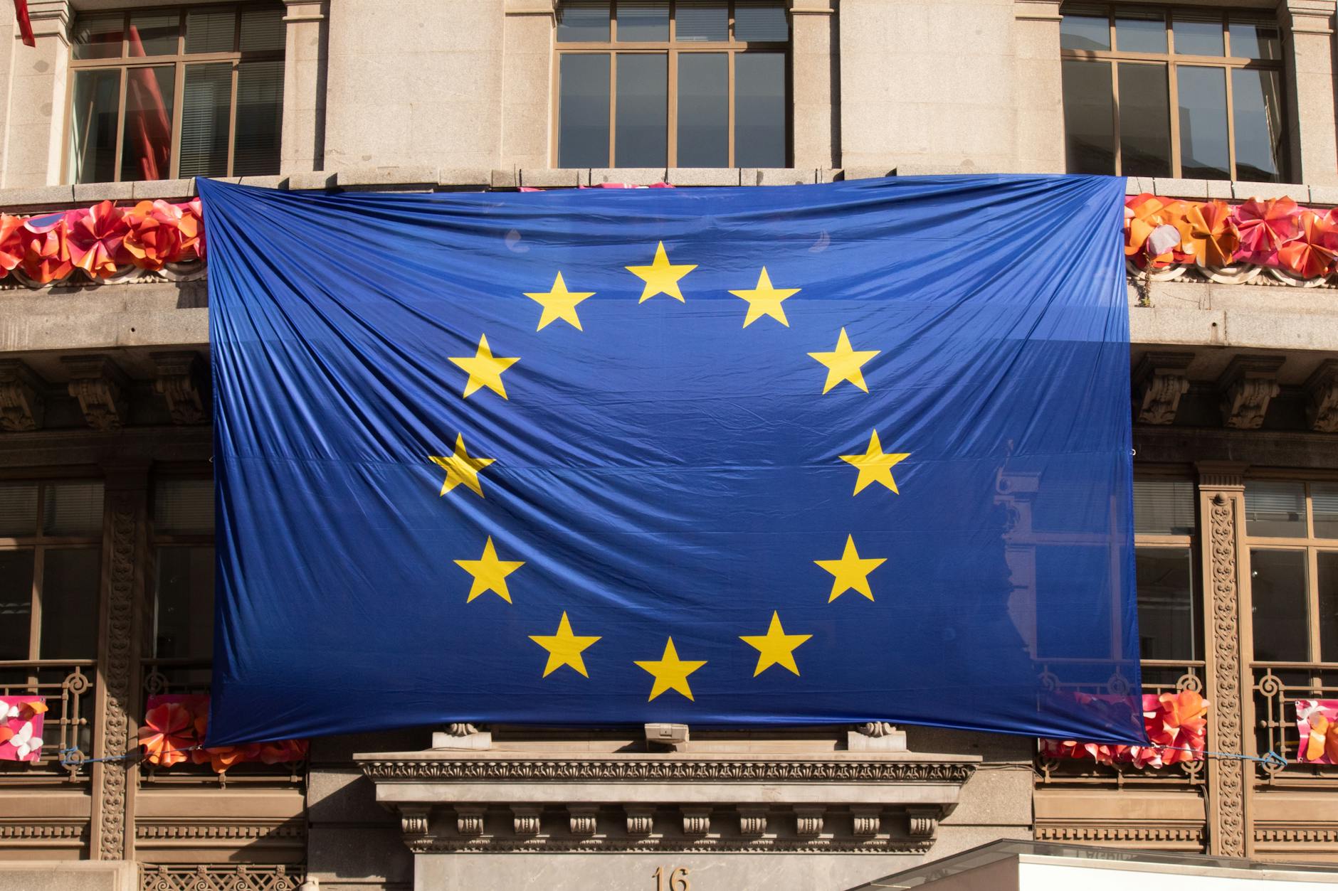 Large European Union flag draped over a building facade adorned with festive decorations.