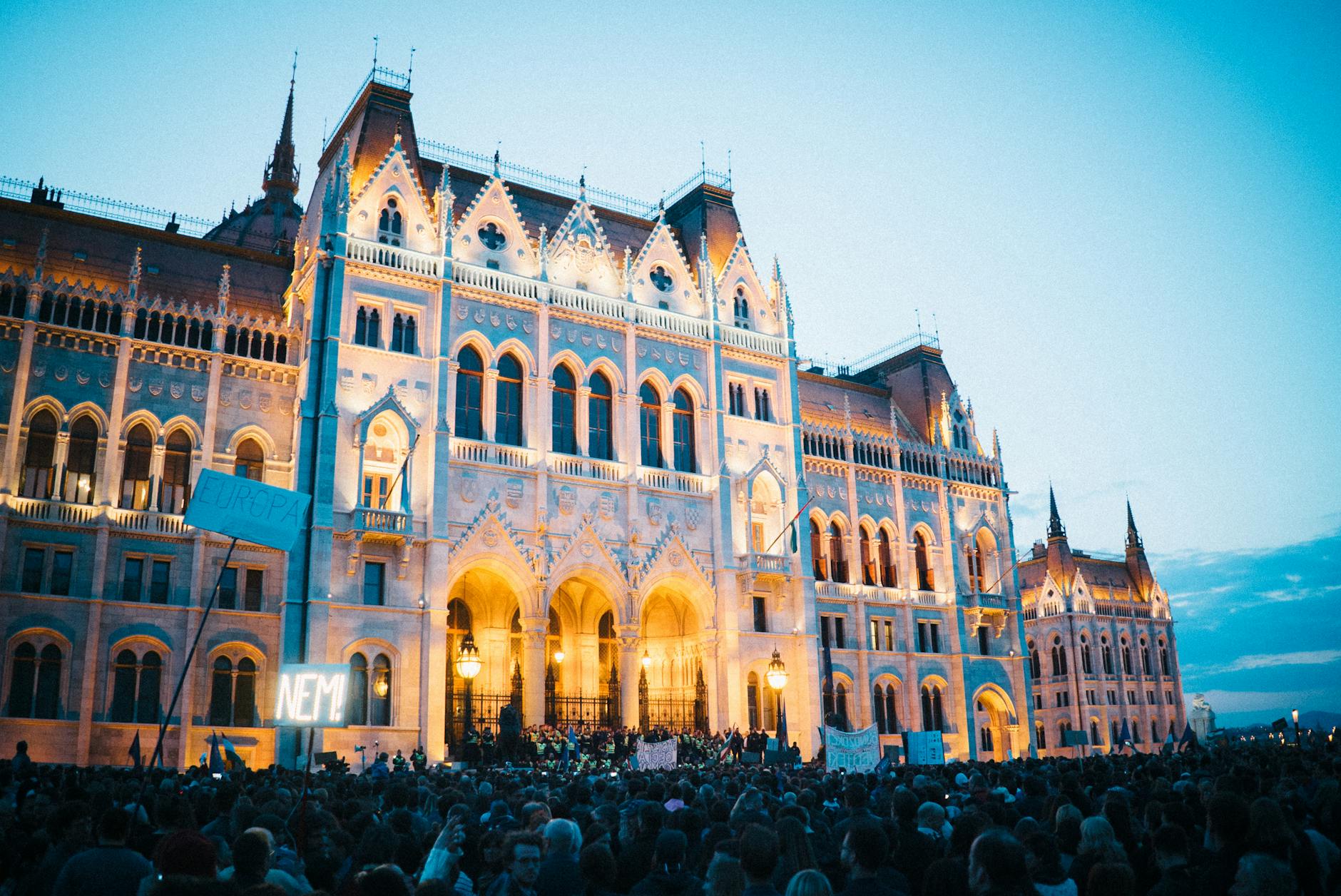 Crowd of protesters gathered in front of the historic Budapest Parliament Building during the evening.