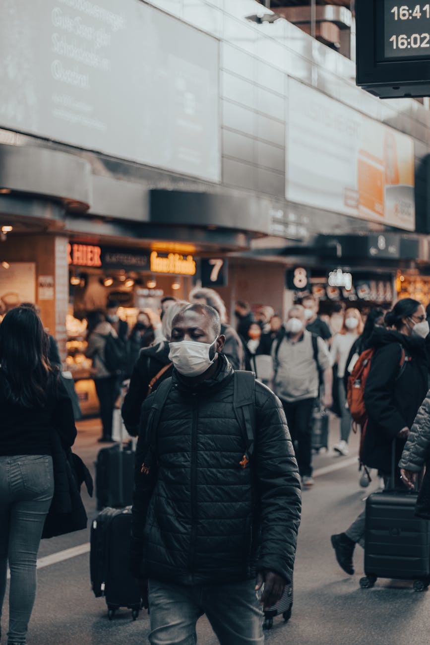A busy airport scene with travelers wearing masks and carrying luggage.