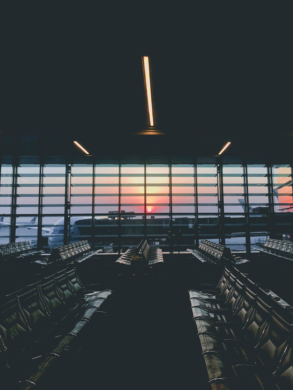 A serene view of an empty airport terminal during sunset, overlooking parked airplanes through large windows.