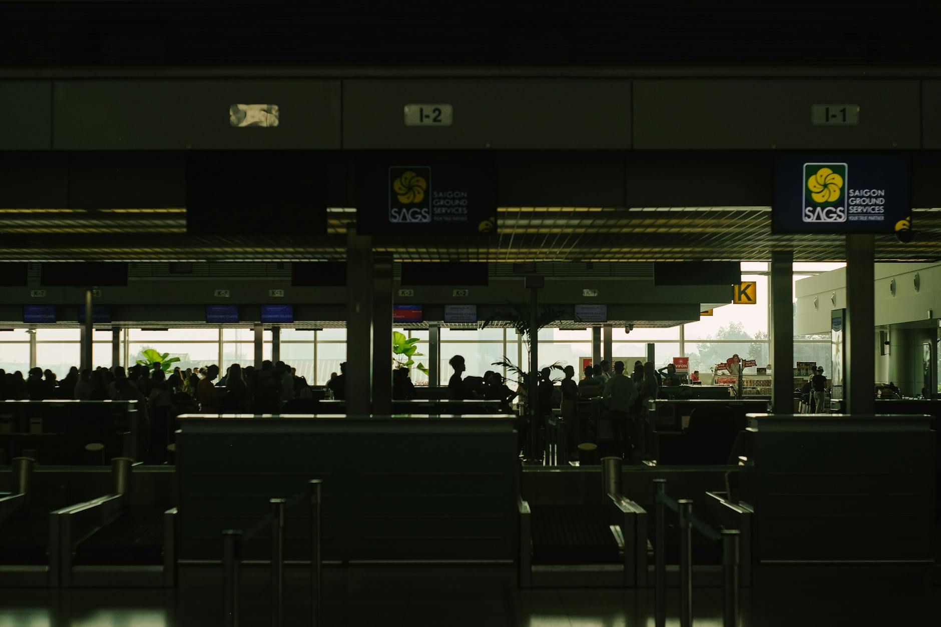 Silhouetted travelers wait at a bustling airport check-in counter, showcasing Saigon Ground Services.