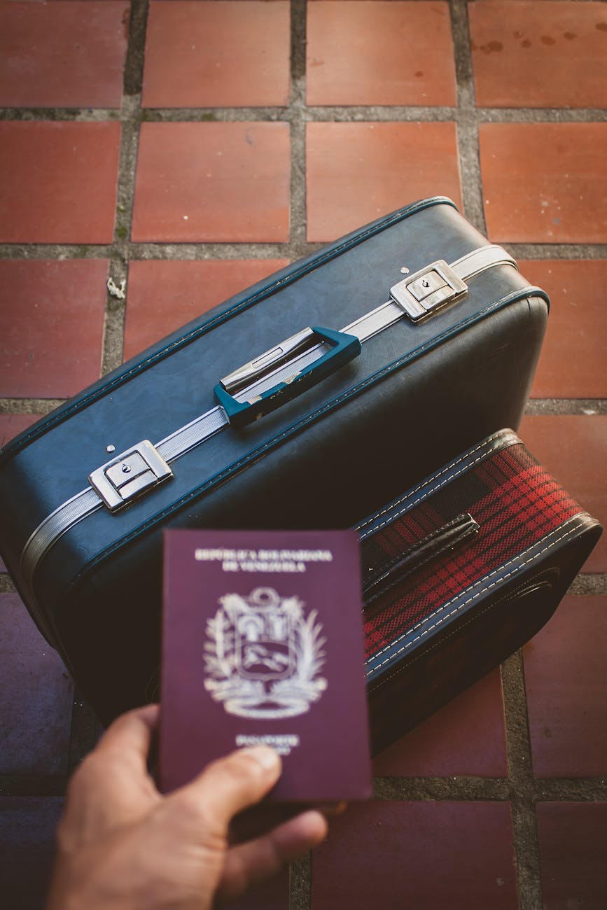 A traveler's essentials including a passport and suitcase on a red tiled floor, suggesting a journey ahead.