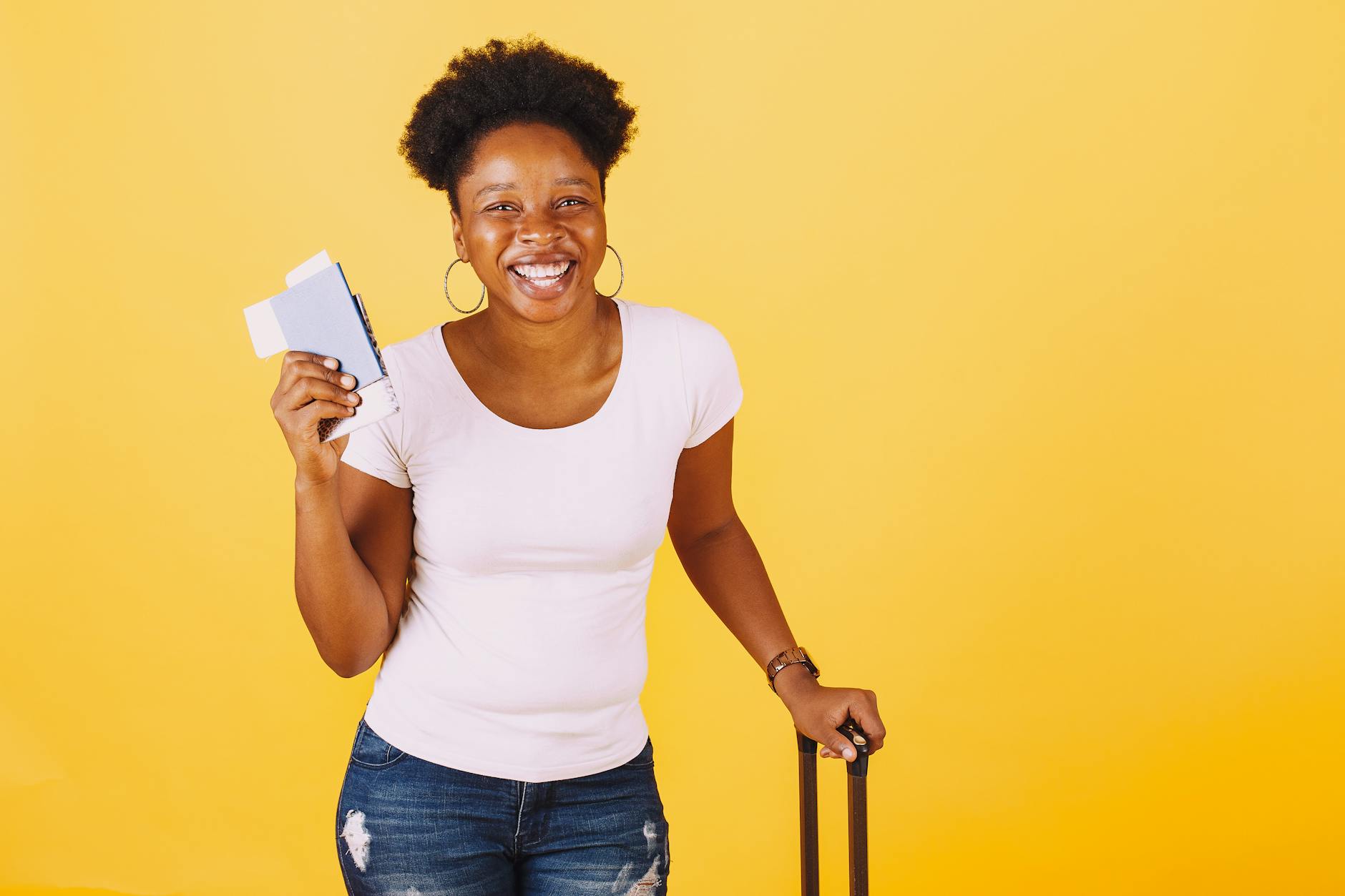 Cheerful woman holding passport ready for travel against a vibrant yellow backdrop.