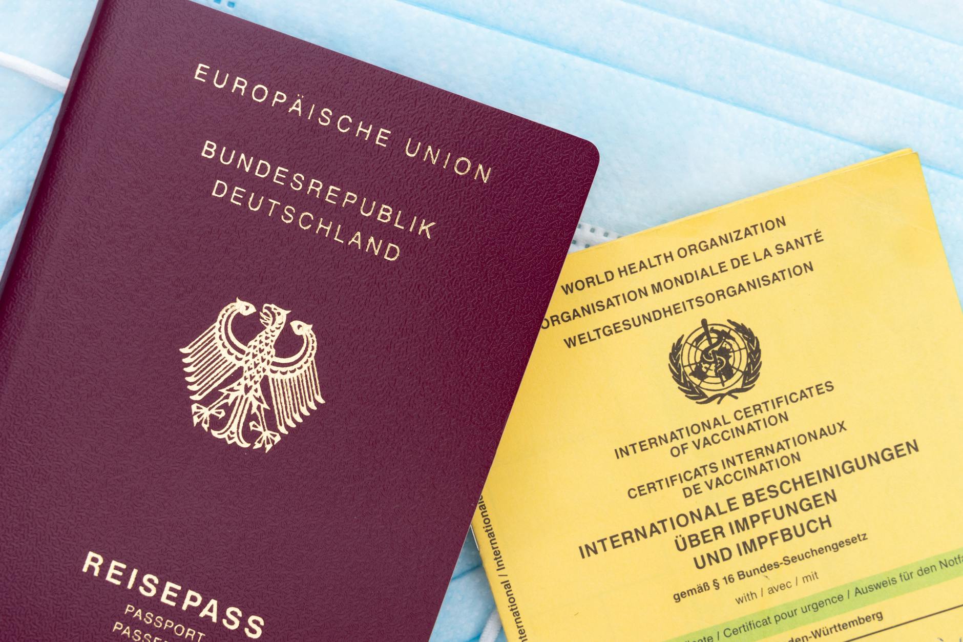 Close-up of a German passport, vaccination card, and face mask, symbolizing travel and health documentation.