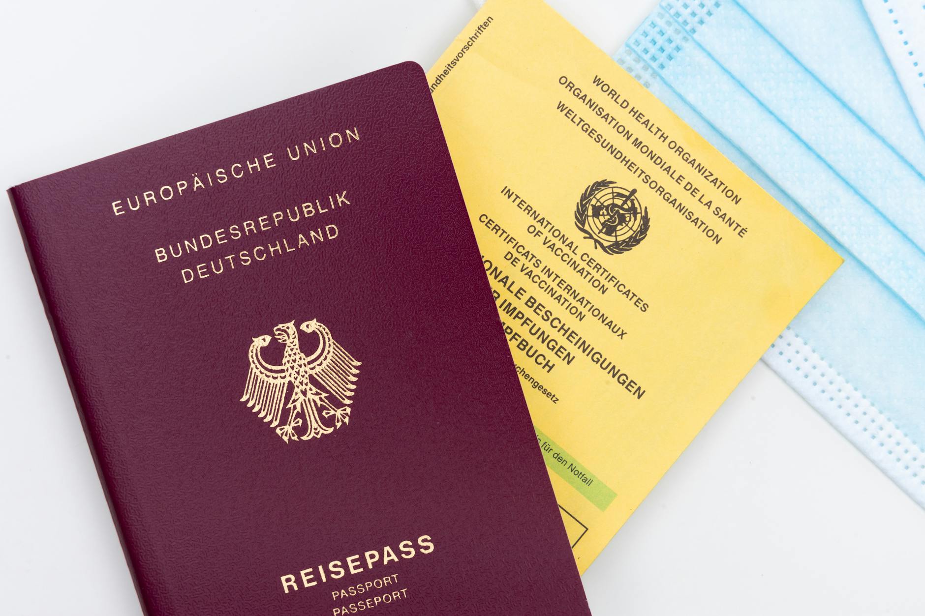 Close-up of a German passport, vaccination card, and mask, symbolizing travel and health safety.