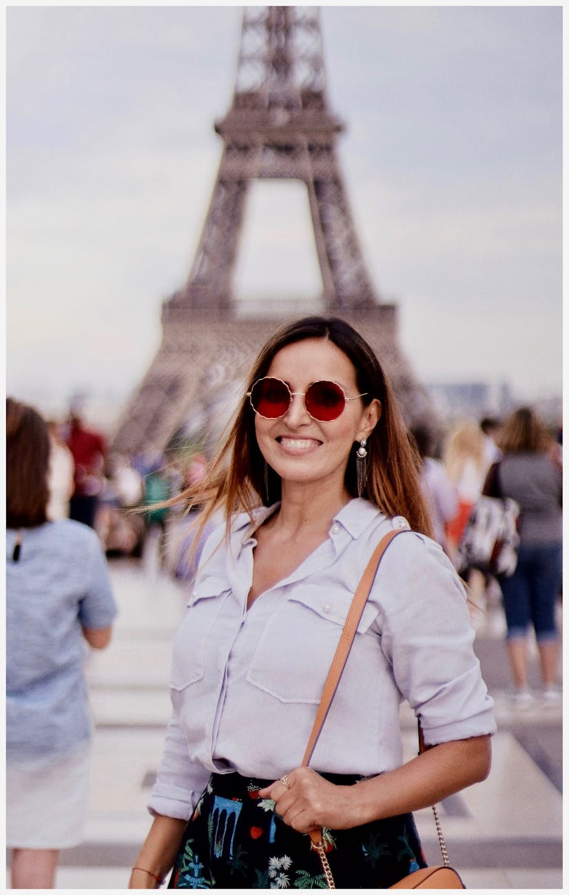 Woman enjoying Paris vacation at Eiffel Tower, France with a joyful smile and casual summer attire.