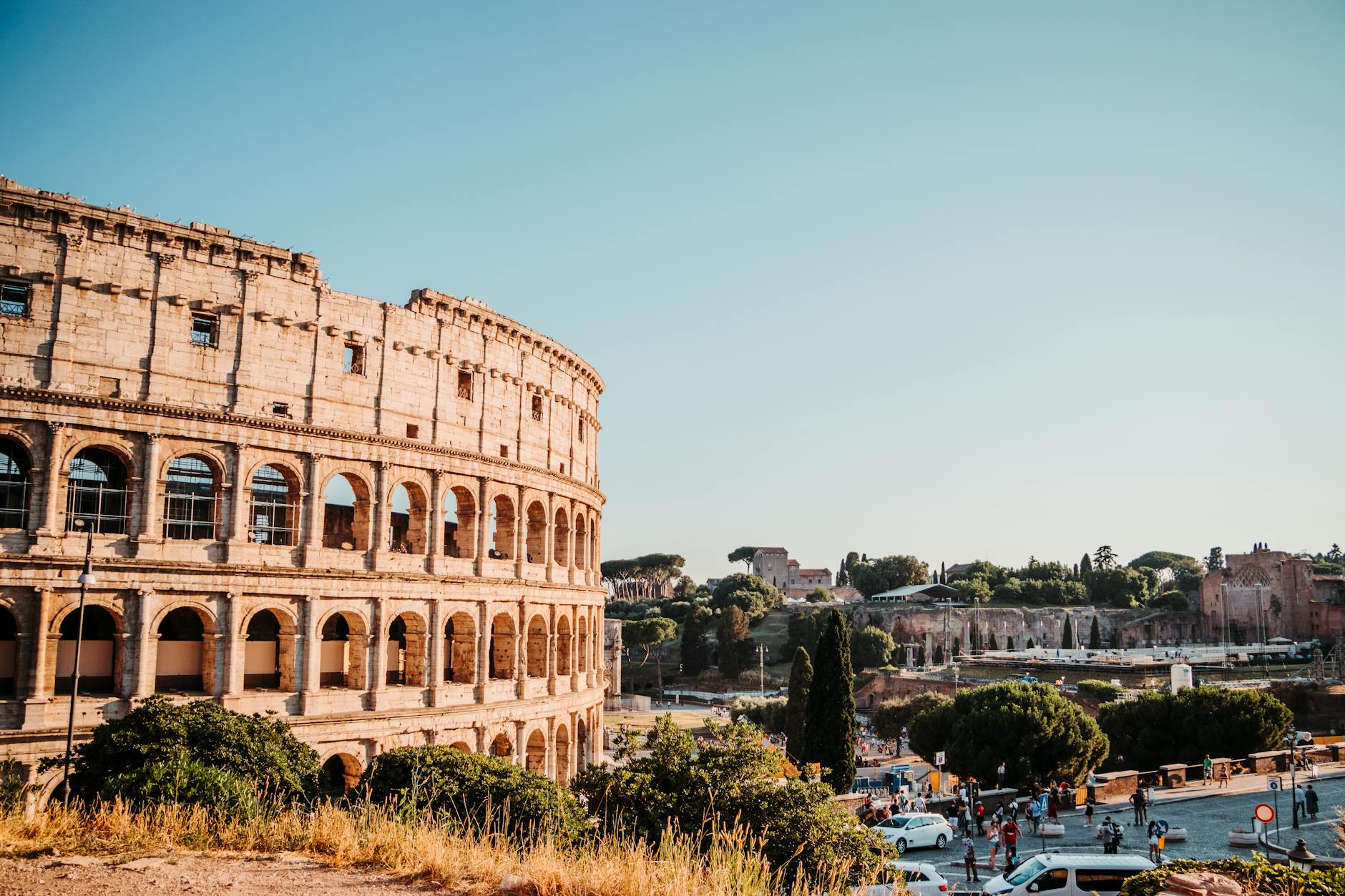 The iconic Colosseum in Rome, a historic amphitheater surrounded by urban scenery on a bright day.