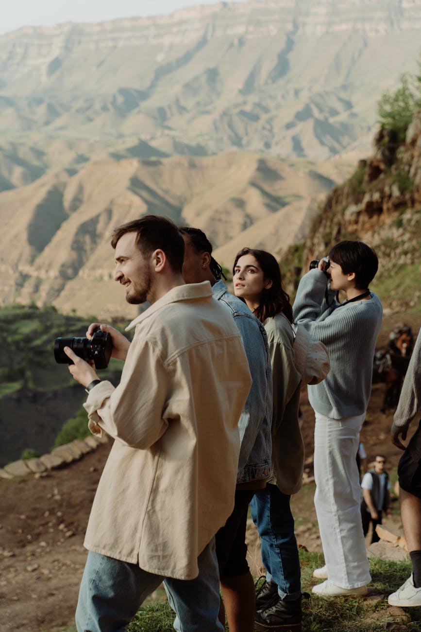 A group of tourists observes and photographs stunning mountain views at sunset.