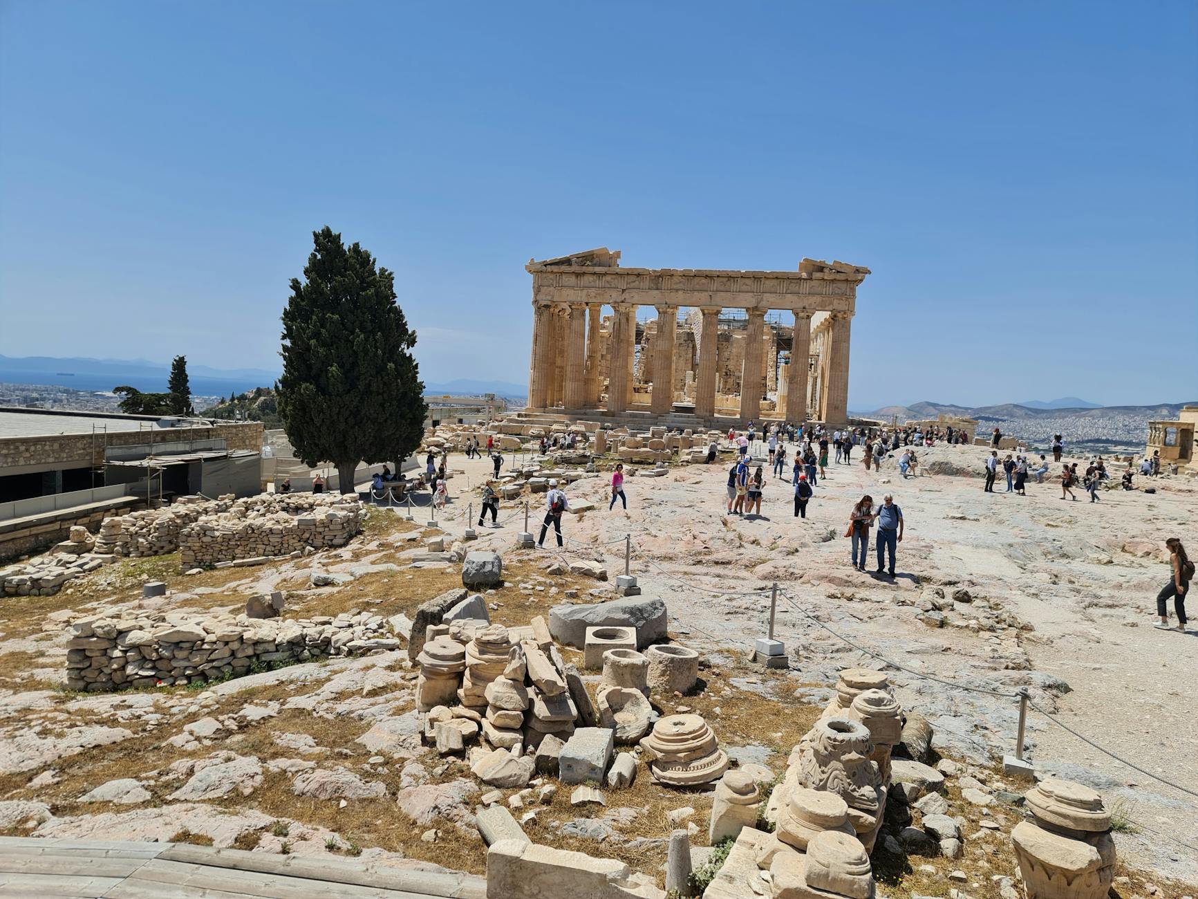 Tourists wander around the iconic Parthenon on a sunny day, exploring its ancient ruins.