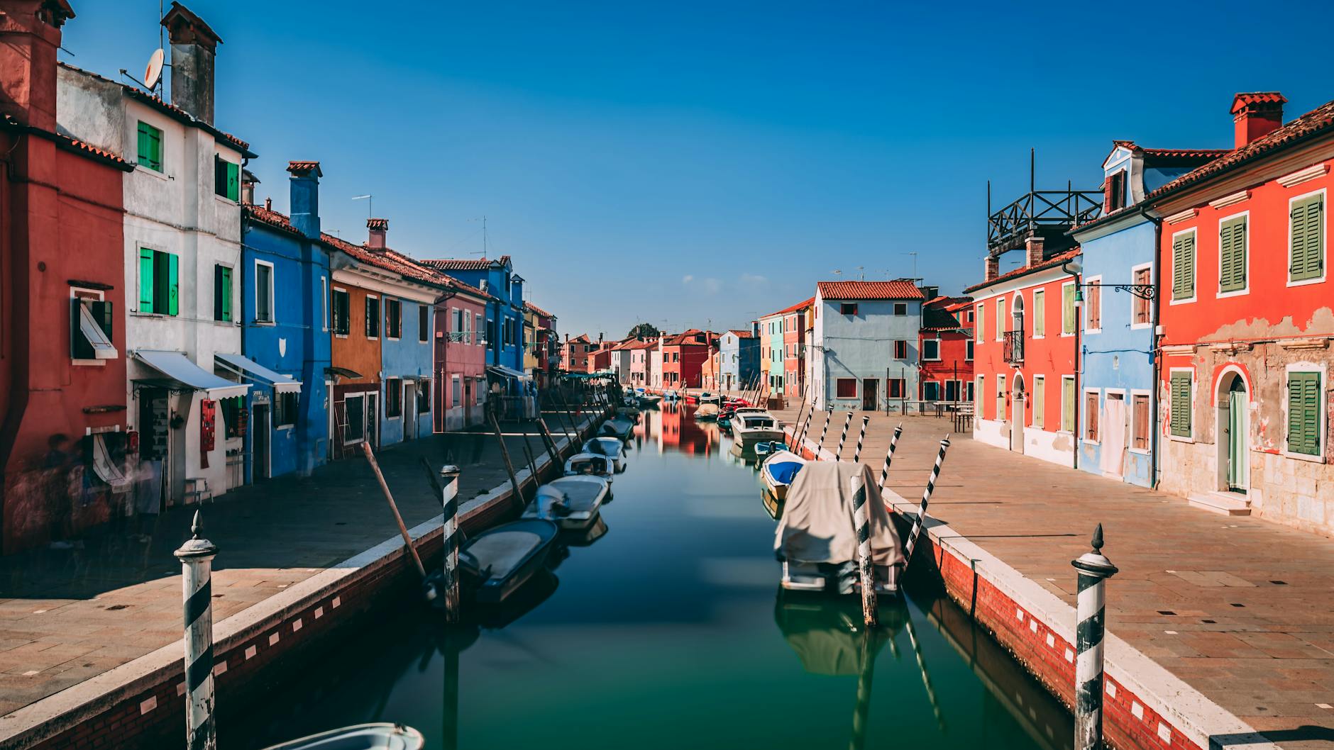 Vibrant houses lining a tranquil canal in Burano, Venice, Italy.