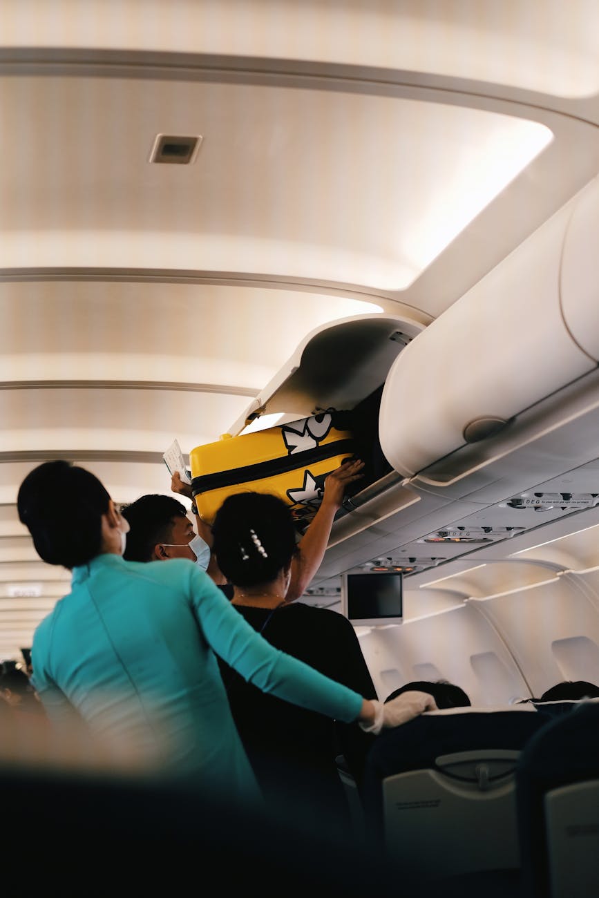 Passengers placing a yellow suitcase in the overhead bin of an airplane cabin. Interior with crew assistance.