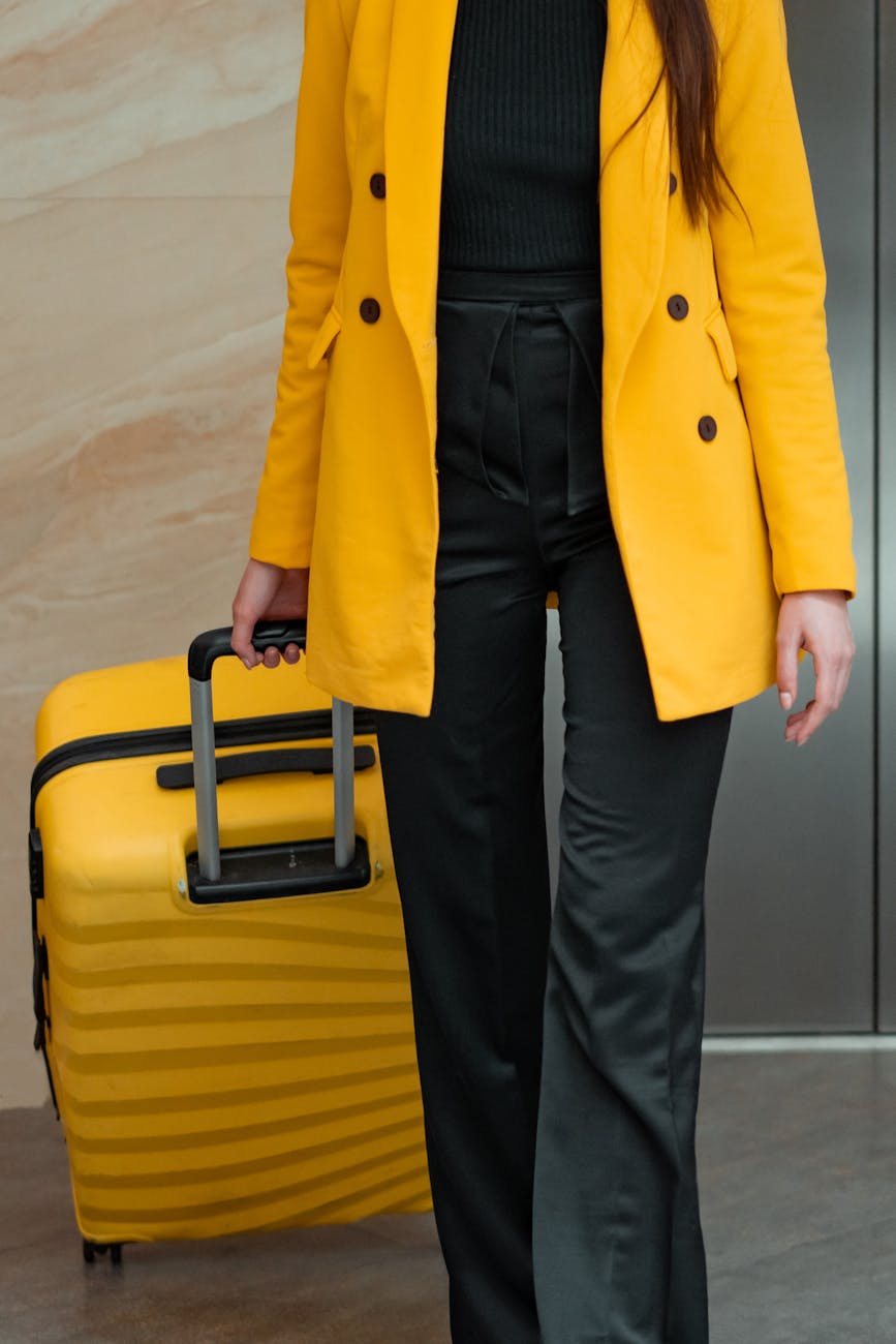 Woman in yellow coat with rolling luggage, ready for travel. A modern fashion and travel concept.