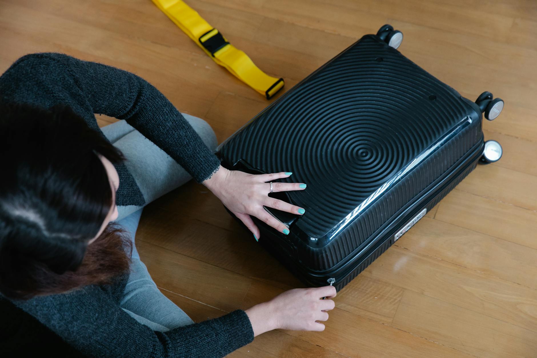 A woman preparing her suitcase for travel, sitting on a wooden floor indoors.
