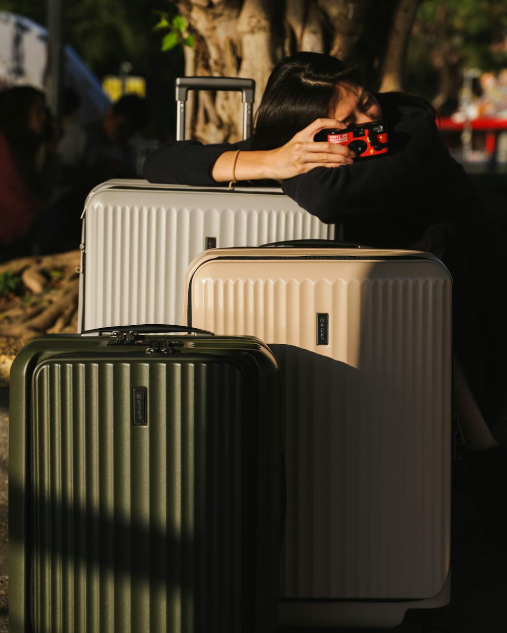 Woman holding a vintage camera while leaning on stacked suitcases outdoors.