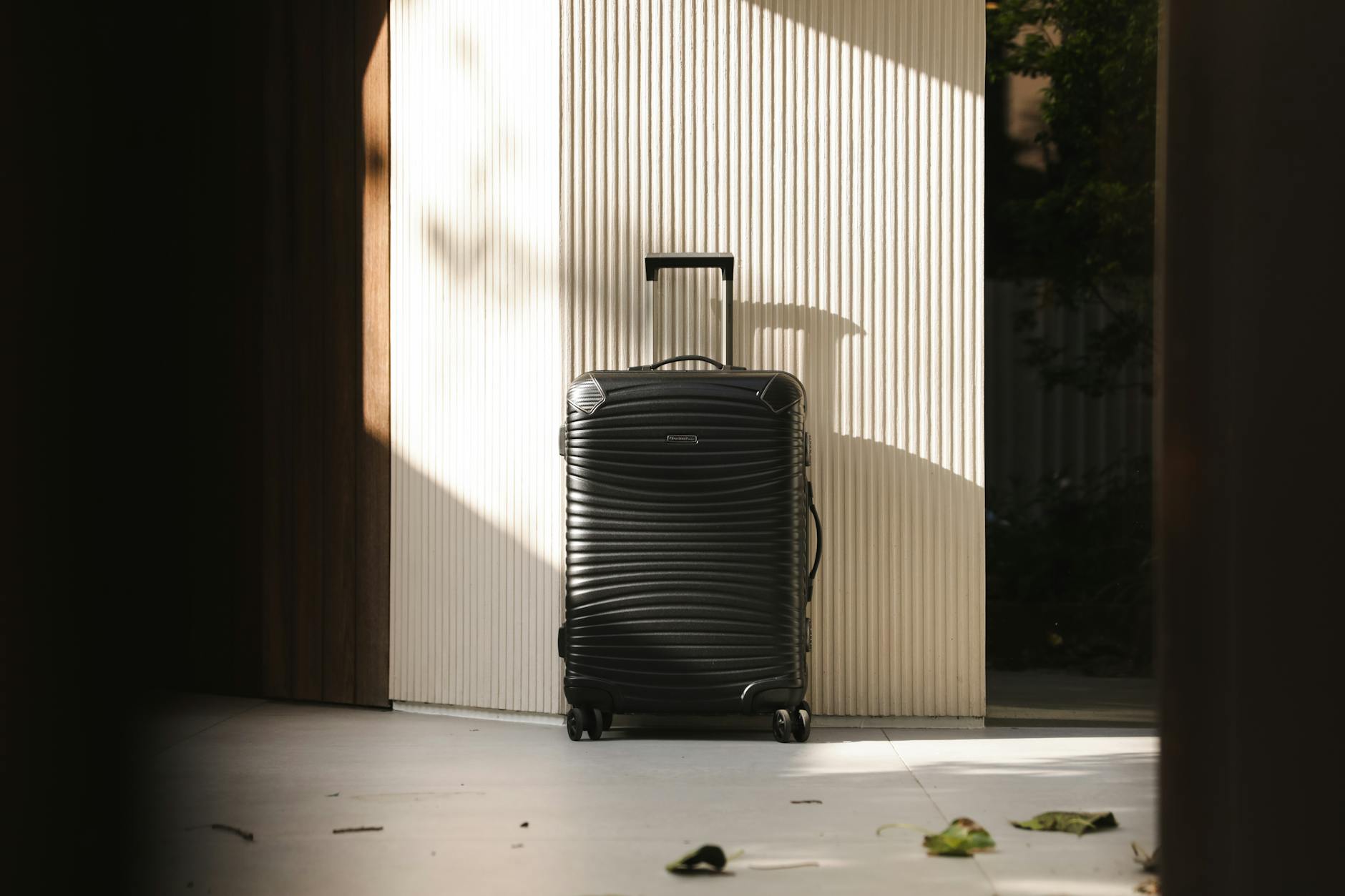A sleek black suitcase stands in a sunlit hallway, capturing travel elegance and simplicity.
