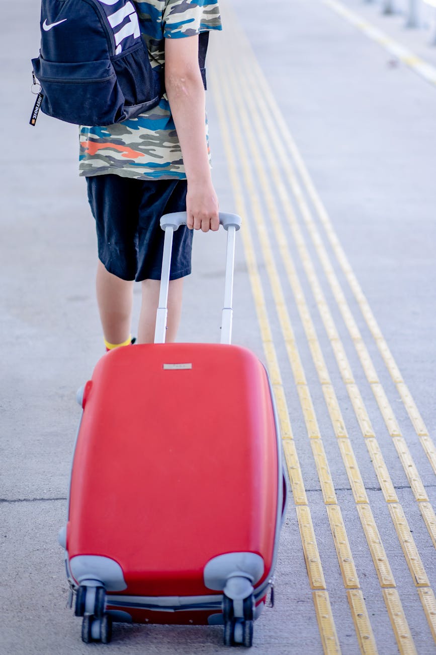 Person with red luggage walking on a sunny outdoor walkway, capturing a travel moment.