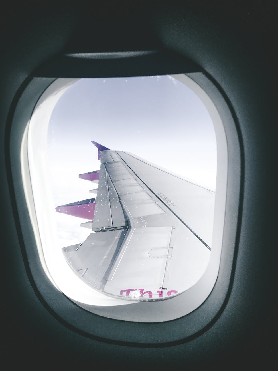 View of an airplane wing through a window, capturing flight over clouds.