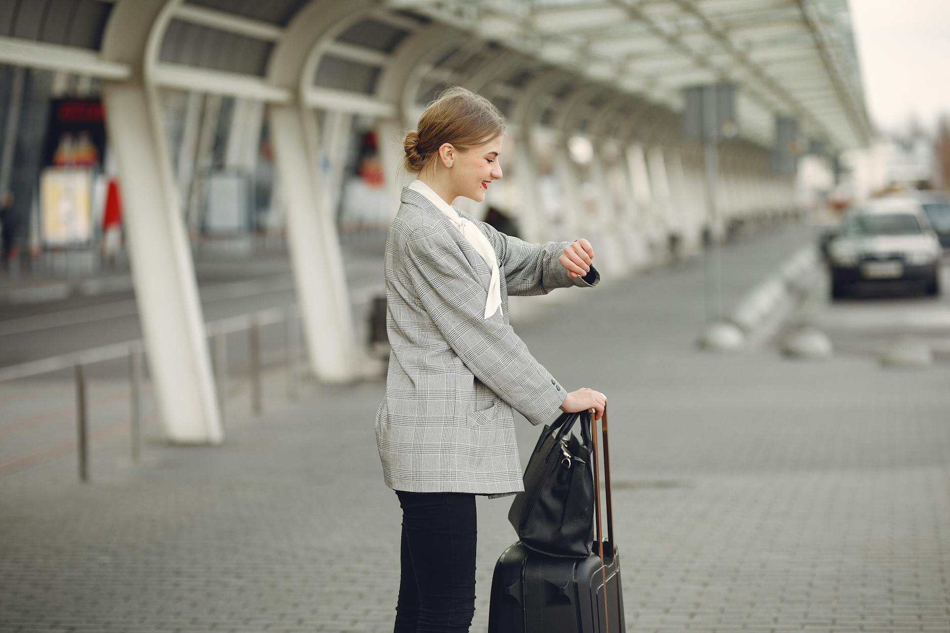 Woman in gray jacket checking wristwatch at station with luggage, representing punctual travel.